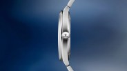 Side view of a slim silver wristwatch case with a ridged crown featuring a logo on a blue gradient background.