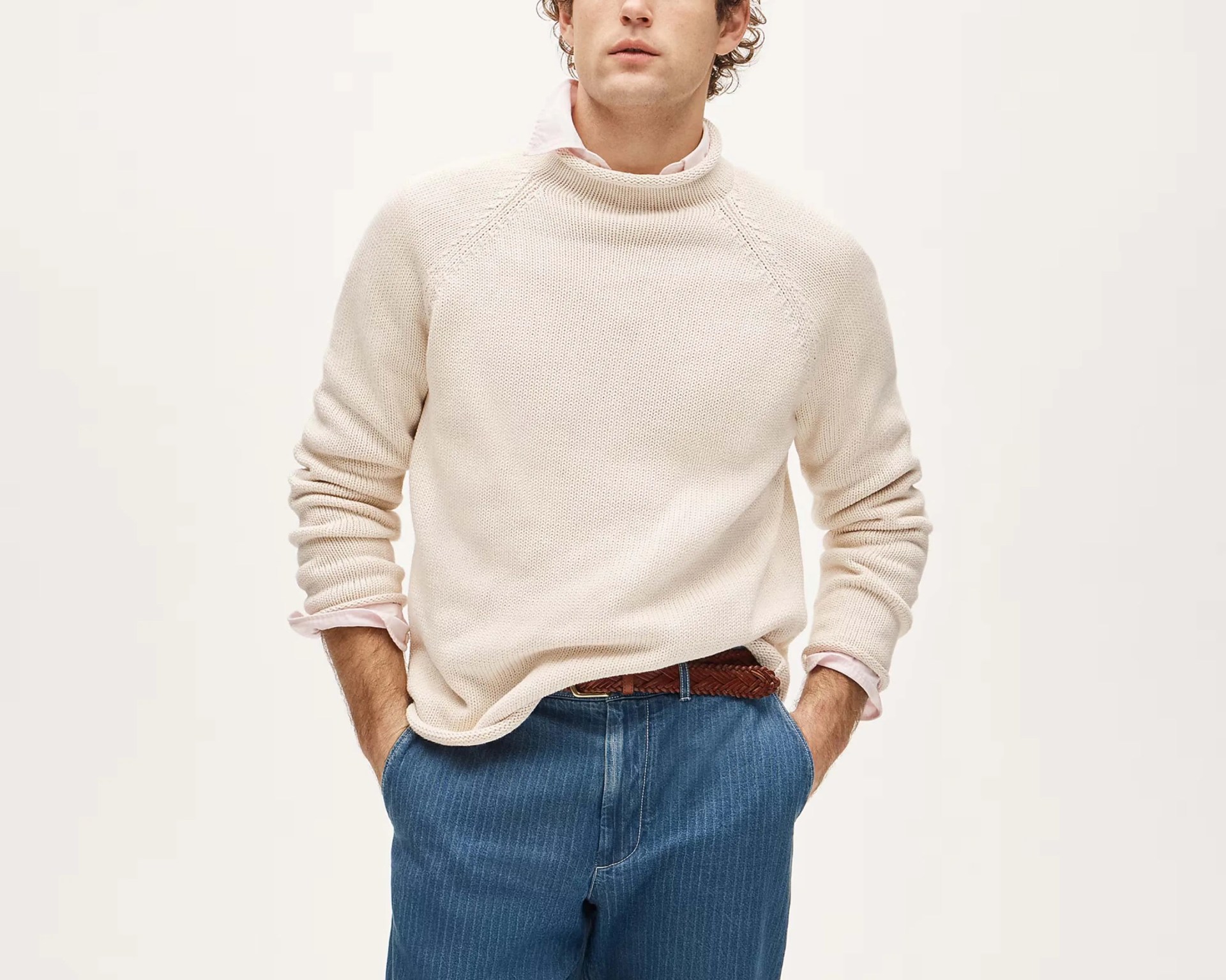 Cream knit sweater worn over a light pink collared shirt tucked into blue pinstriped pants with a brown braided belt.