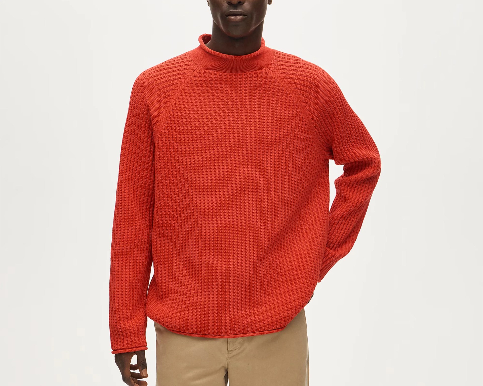 Bright orange textured knit sweater with a mock neck worn with beige pants.