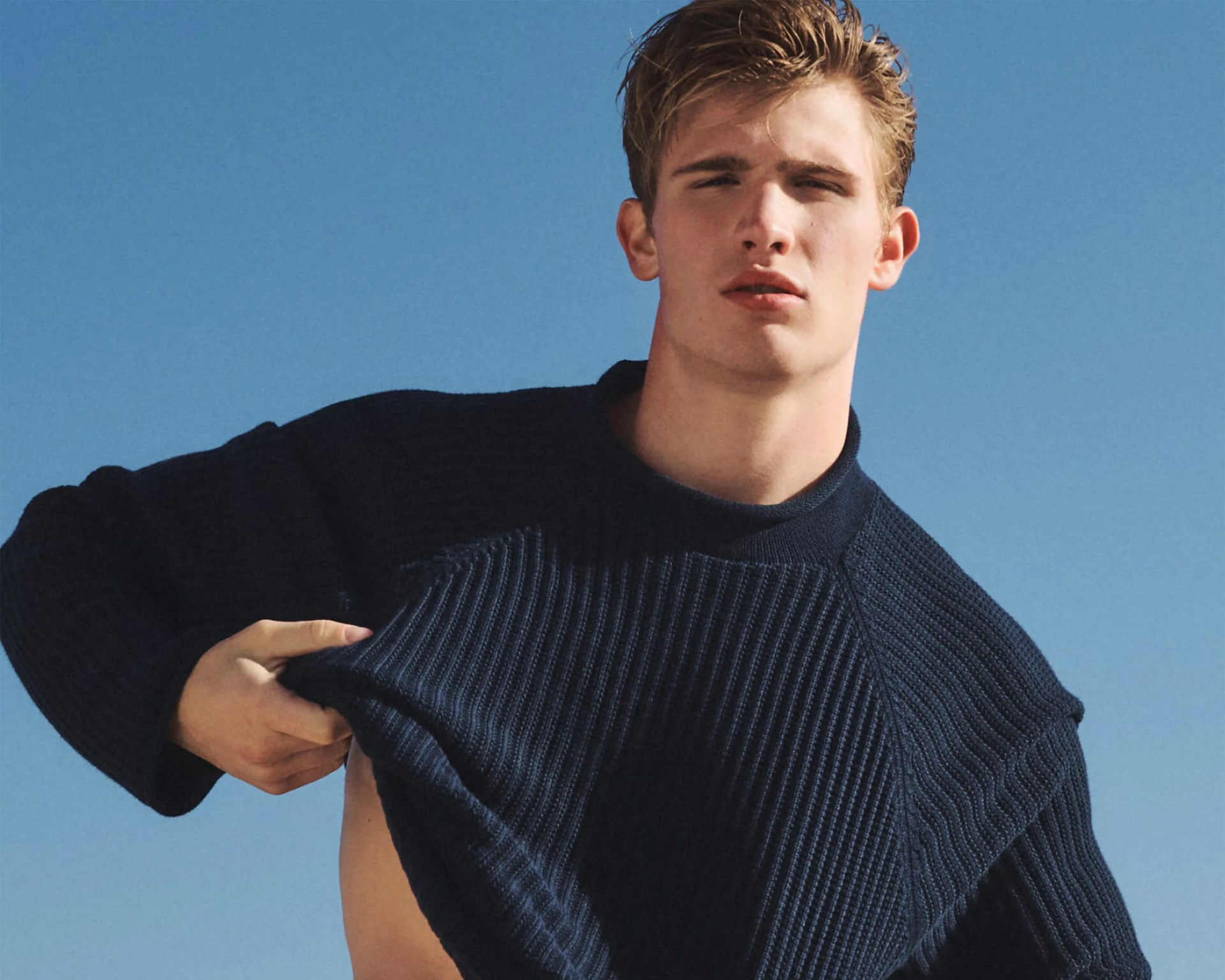 Navy blue ribbed knit sweater held up by a person against a clear blue sky.