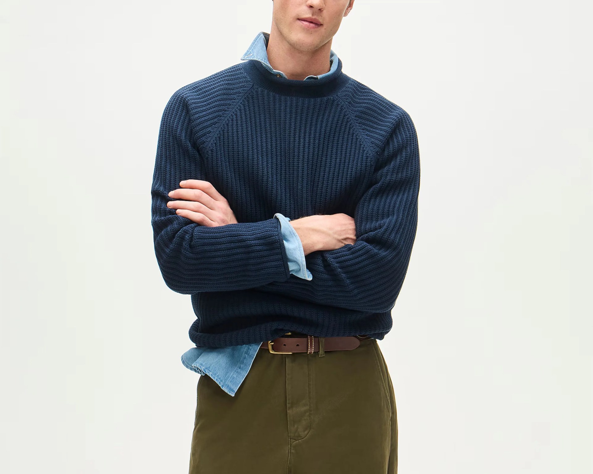 Navy blue ribbed knit sweater layered over a light blue denim shirt with olive green pants and a brown belt.