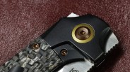 Close-up of a folding knife handle with textured carbon fiber and black metal parts with bronze screws.