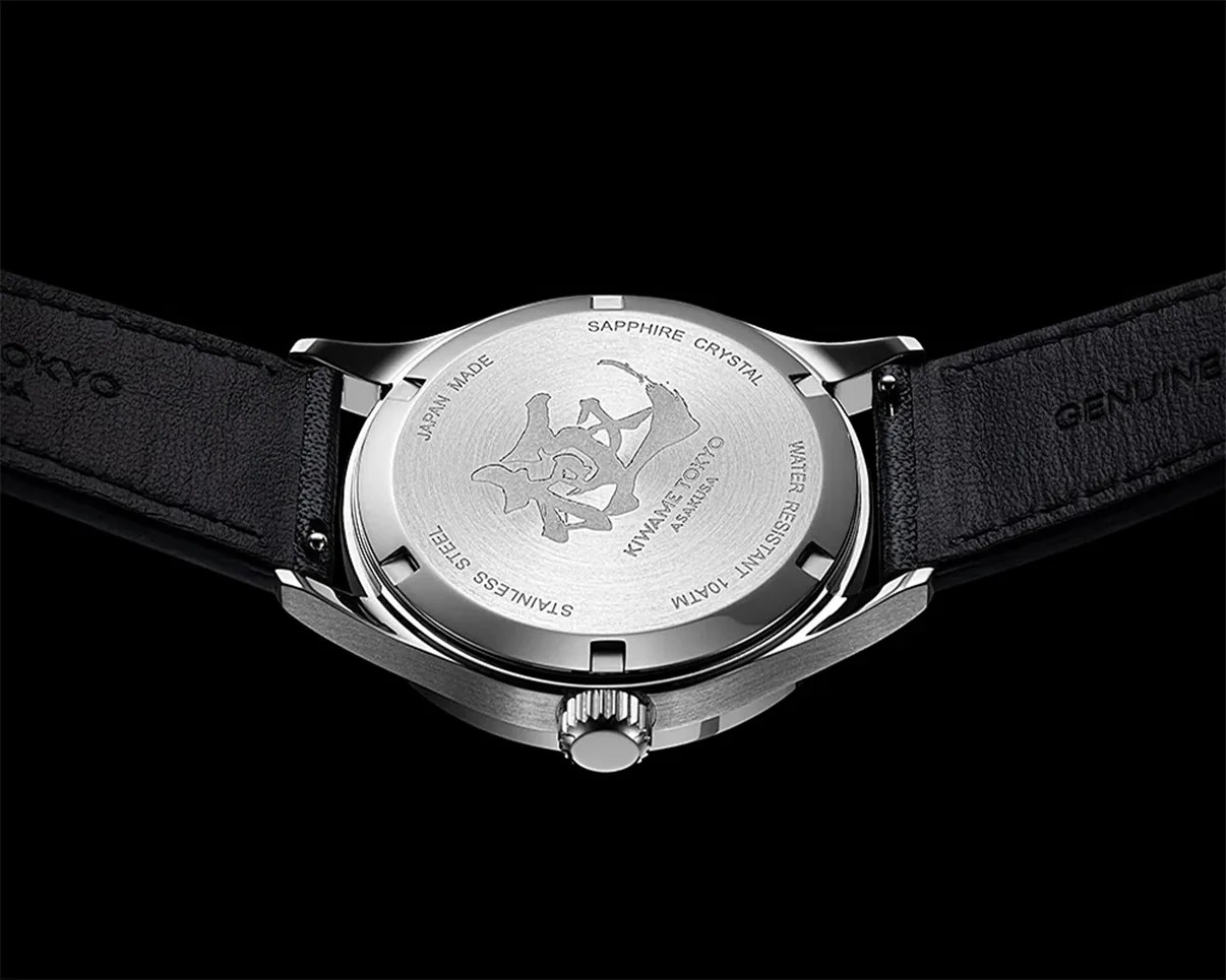Back of a stainless steel wristwatch with black leather strap and engraved Japanese characters on the case back.