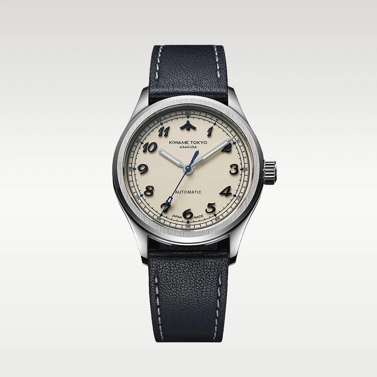 Silver round watch with cream dial, black Arabic numerals, blue hands, and black leather strap with white stitching.