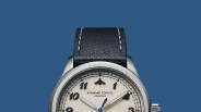 Silver watch with cream dial, black numerals, blue hands, and black leather strap with white stitching.