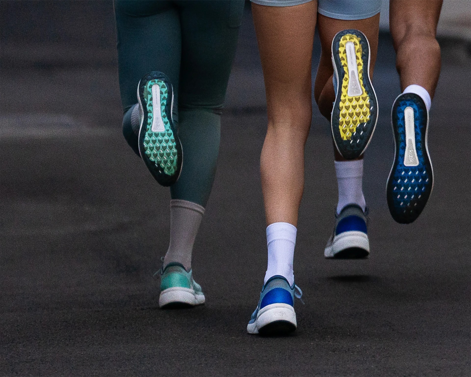 Three people running on a dark road wearing sneakers with green, yellow, and blue patterned soles.