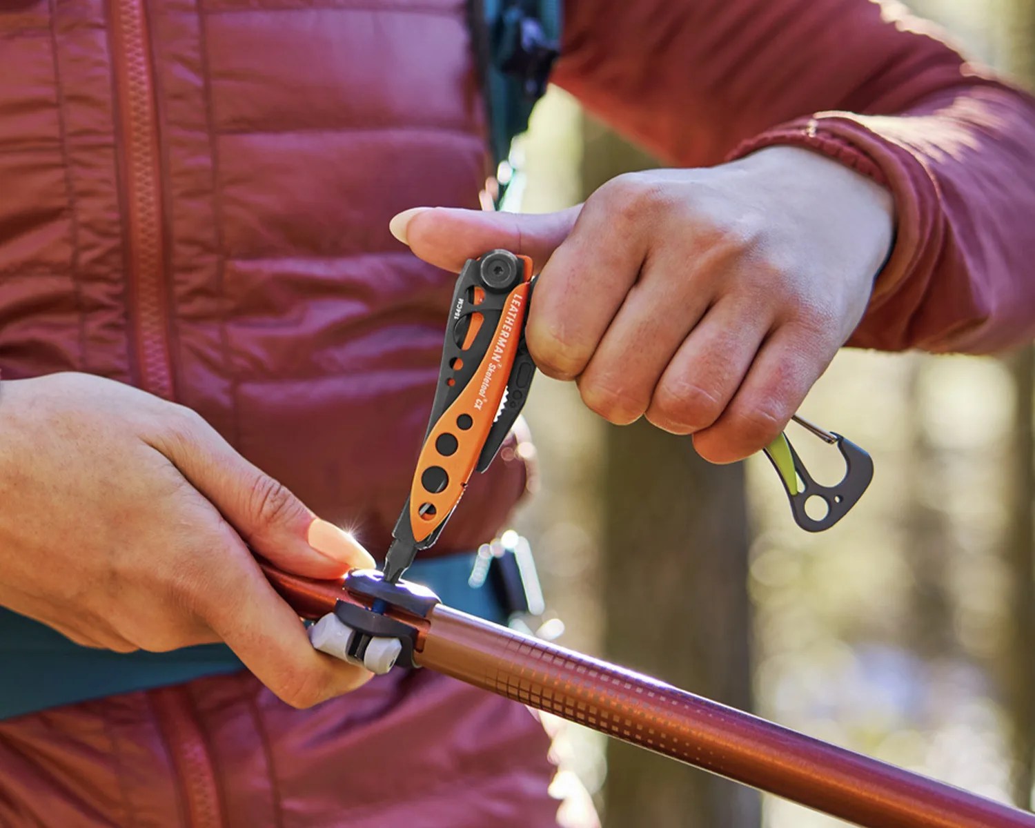 Person in a red jacket using an orange and black Leatherman multitool on a trekking pole.