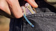 Hand placing a silver and gold multitool with a clip into a dark denim pocket.
