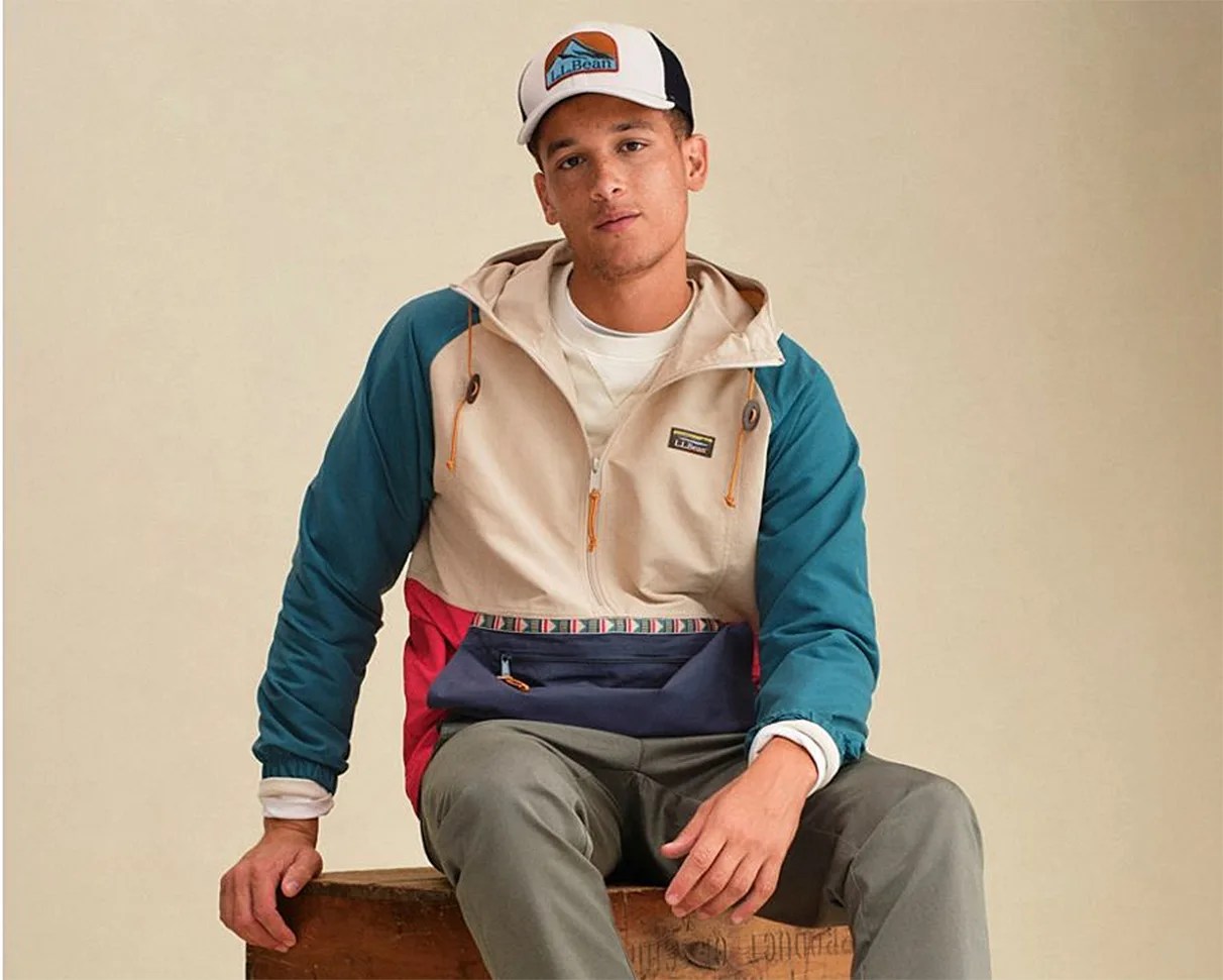 Man wearing a beige, teal, red, and navy color-blocked hooded jacket with a front zipper and a white L.L.Bean cap.
