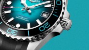 Close-up of a stainless steel watch with a turquoise dial, black bezel with blue markings, and a date window showing "23".