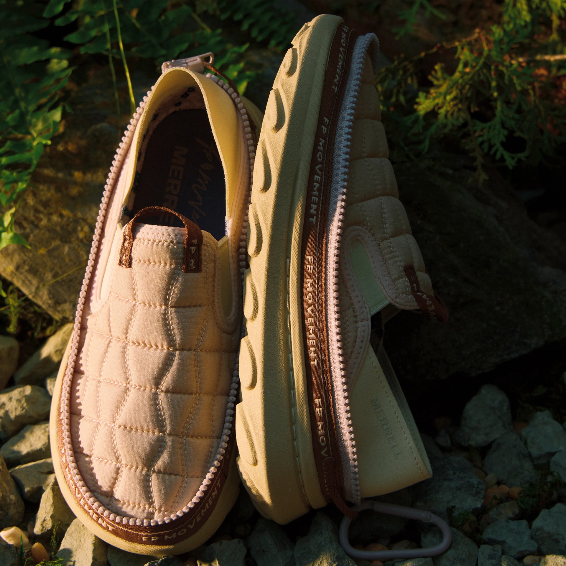Beige quilted slip-on shoes with thick soles and zippers, placed on rocky ground with greenery.
