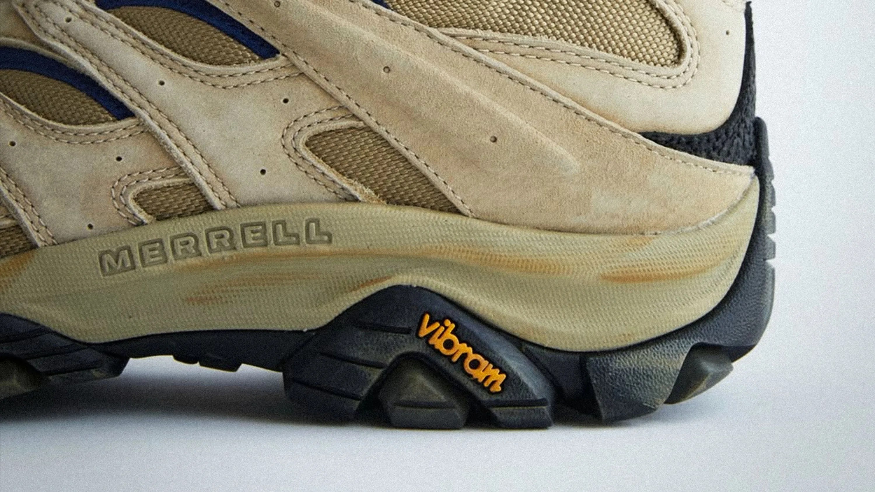 Close-up of beige Merrell hiking shoe with Vibram black sole and orange logo.
