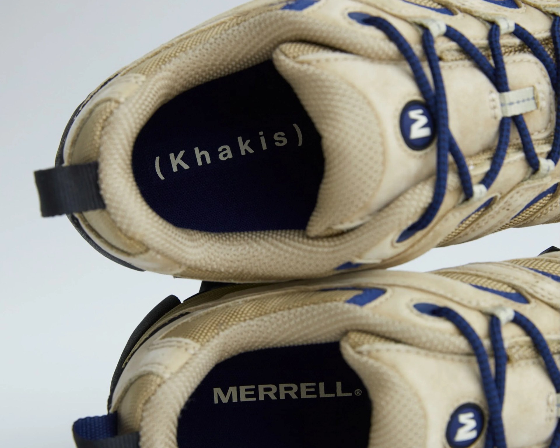 Pair of khaki Merrell sneakers with blue laces viewed from above showing insoles.
