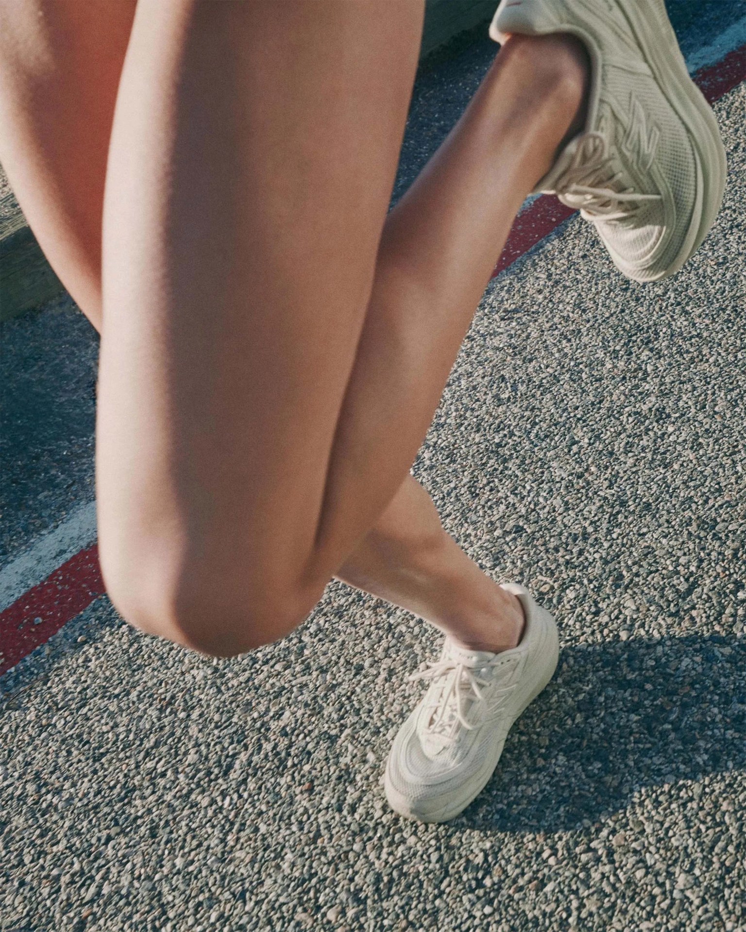 Person wearing off-white New Balance sneakers standing on a textured asphalt surface with a red and white painted line.
