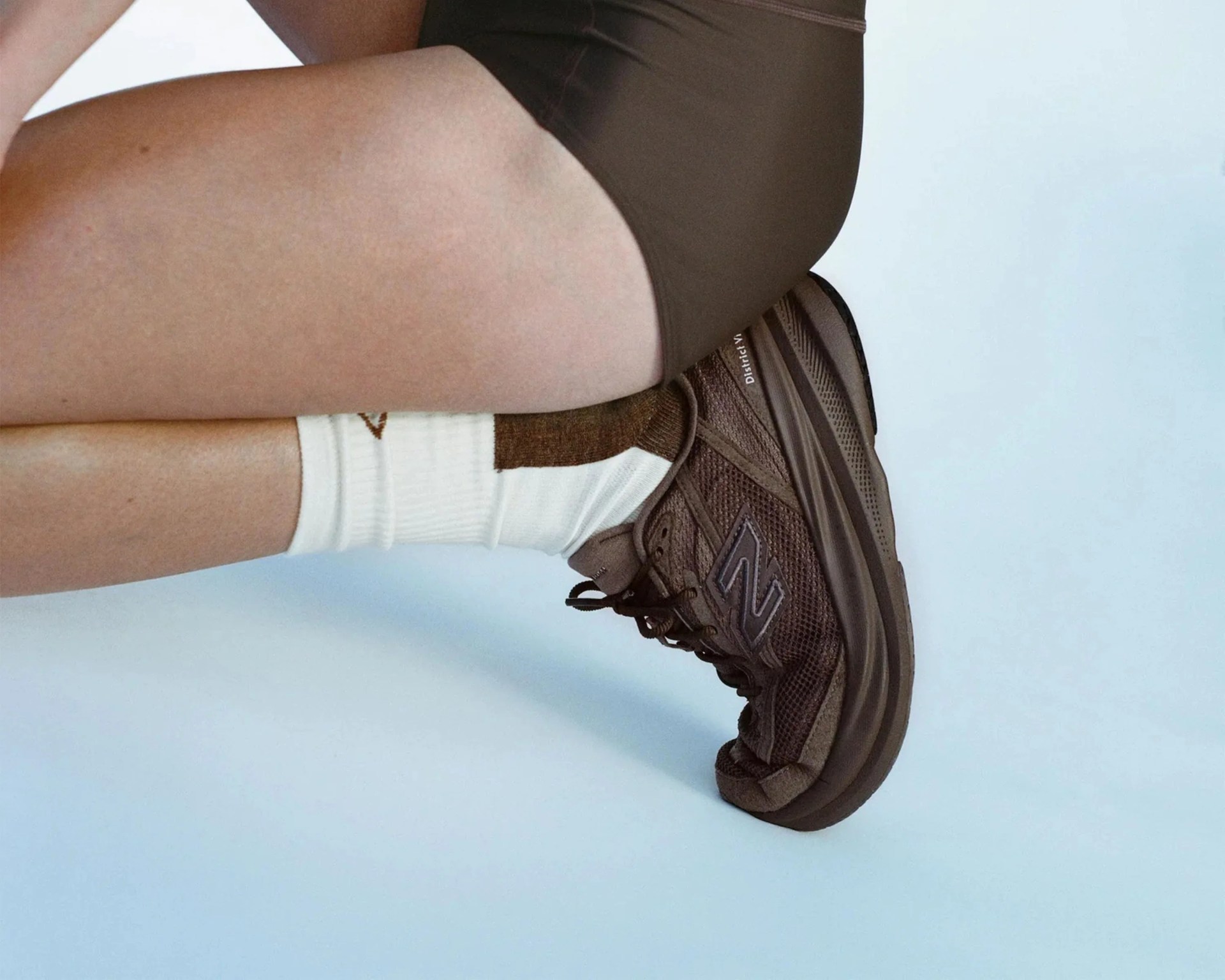 Brown New Balance sneaker with mesh and suede details worn with white and brown socks.