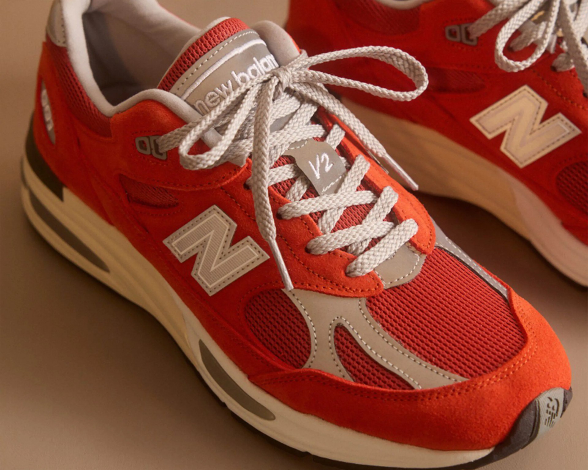Pair of red and gray New Balance sneakers with white laces and cushioned white soles.