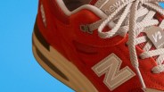 Red New Balance sneaker with white laces and beige midsole against a blue background.