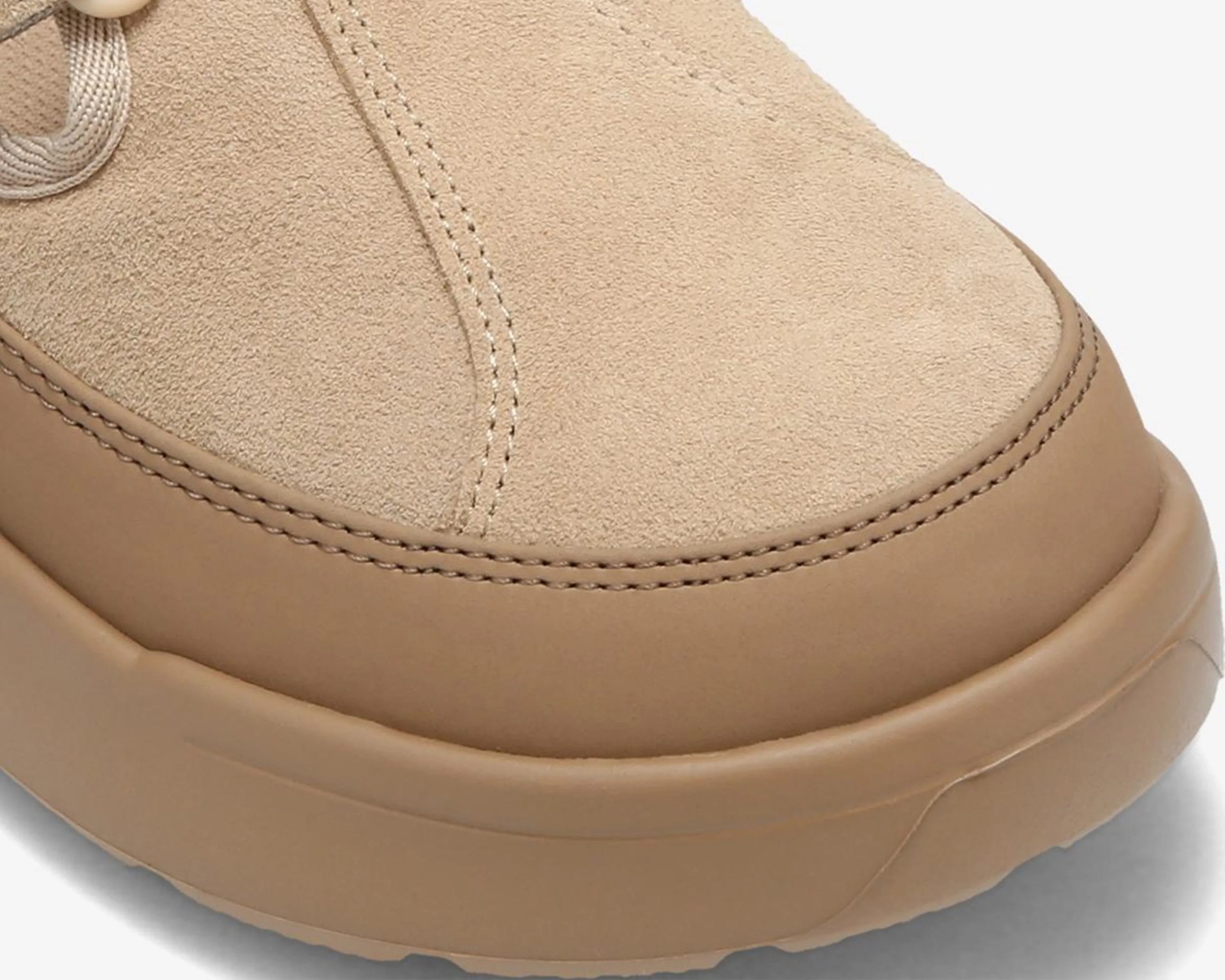 Close-up of a beige suede shoe toe with detailed stitching and a rubber sole.