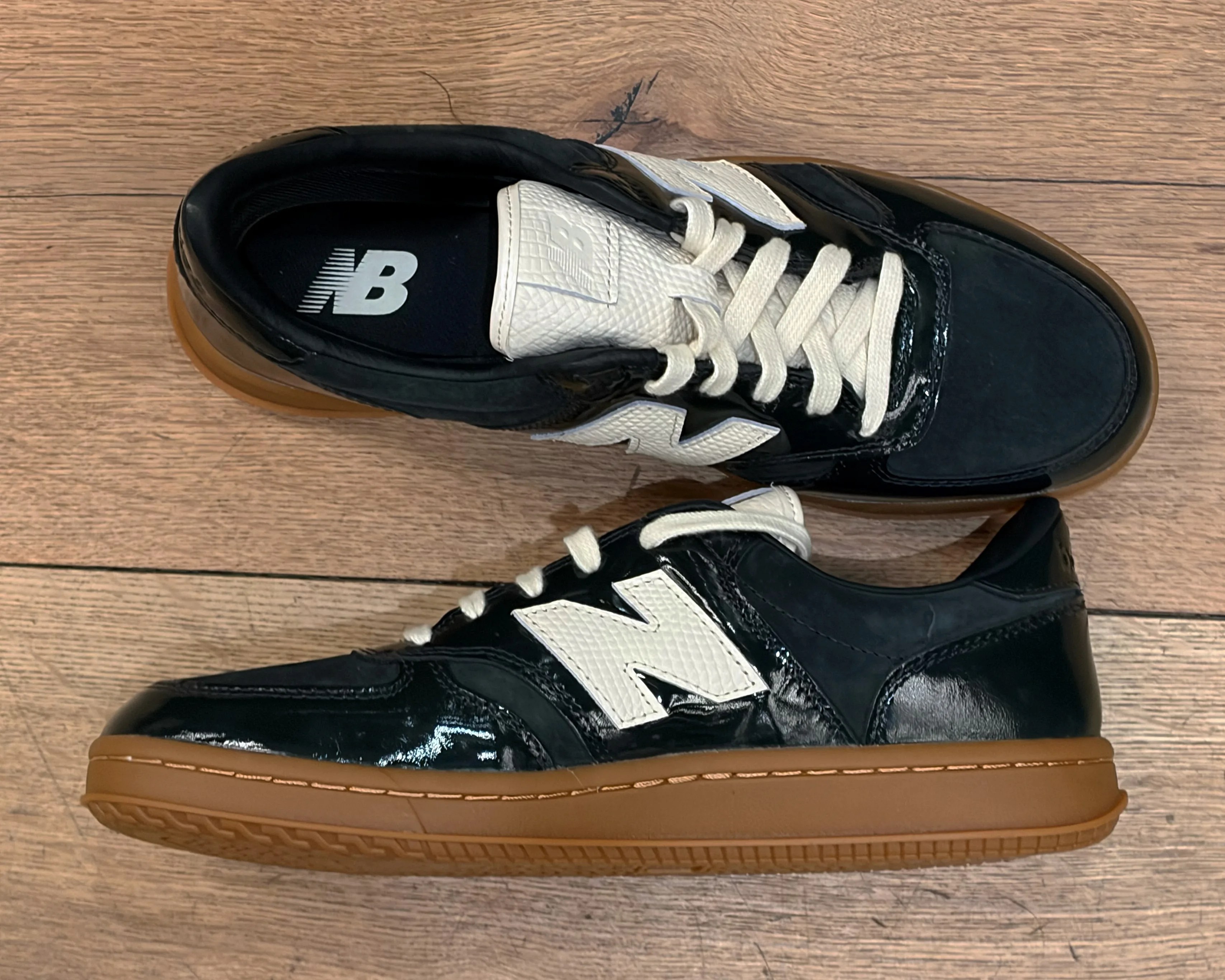 Pair of black and white New Balance sneakers with gum soles on a wooden floor.
