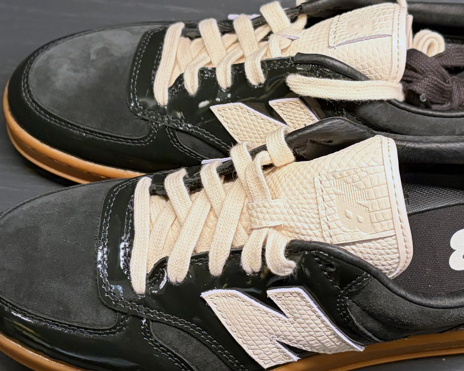 Pair of black and beige New Balance sneakers with textured beige laces and gum soles.