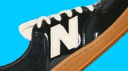 Close-up of a black New Balance sneaker with white laces, a white "N" logo, and a gum sole against a blue background.