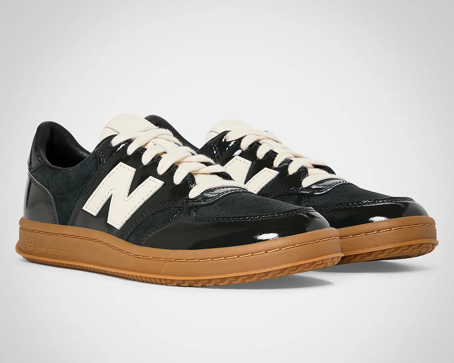 Pair of black New Balance sneakers with white laces and logo, gum rubber sole, and mixed suede and patent leather upper.