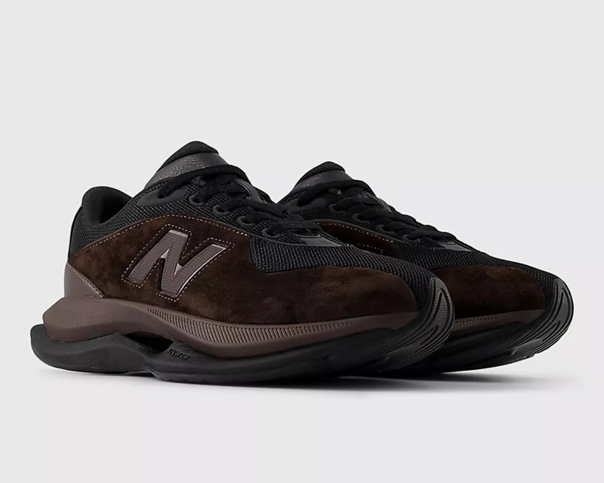 Pair of dark brown and black New Balance sneakers with suede and mesh upper and thick cushioned sole.