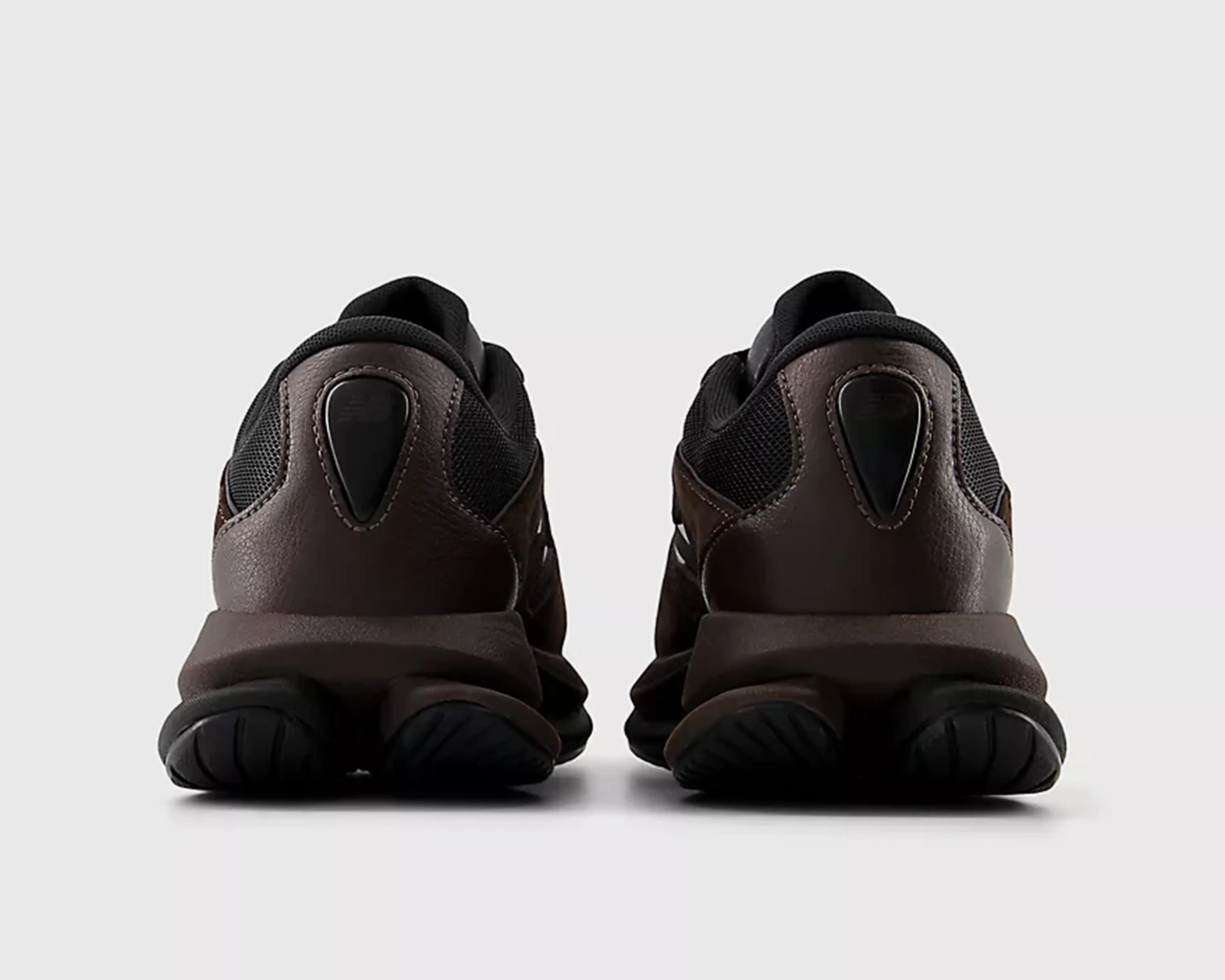 Pair of dark brown and black sneakers shown from the back on a white background.