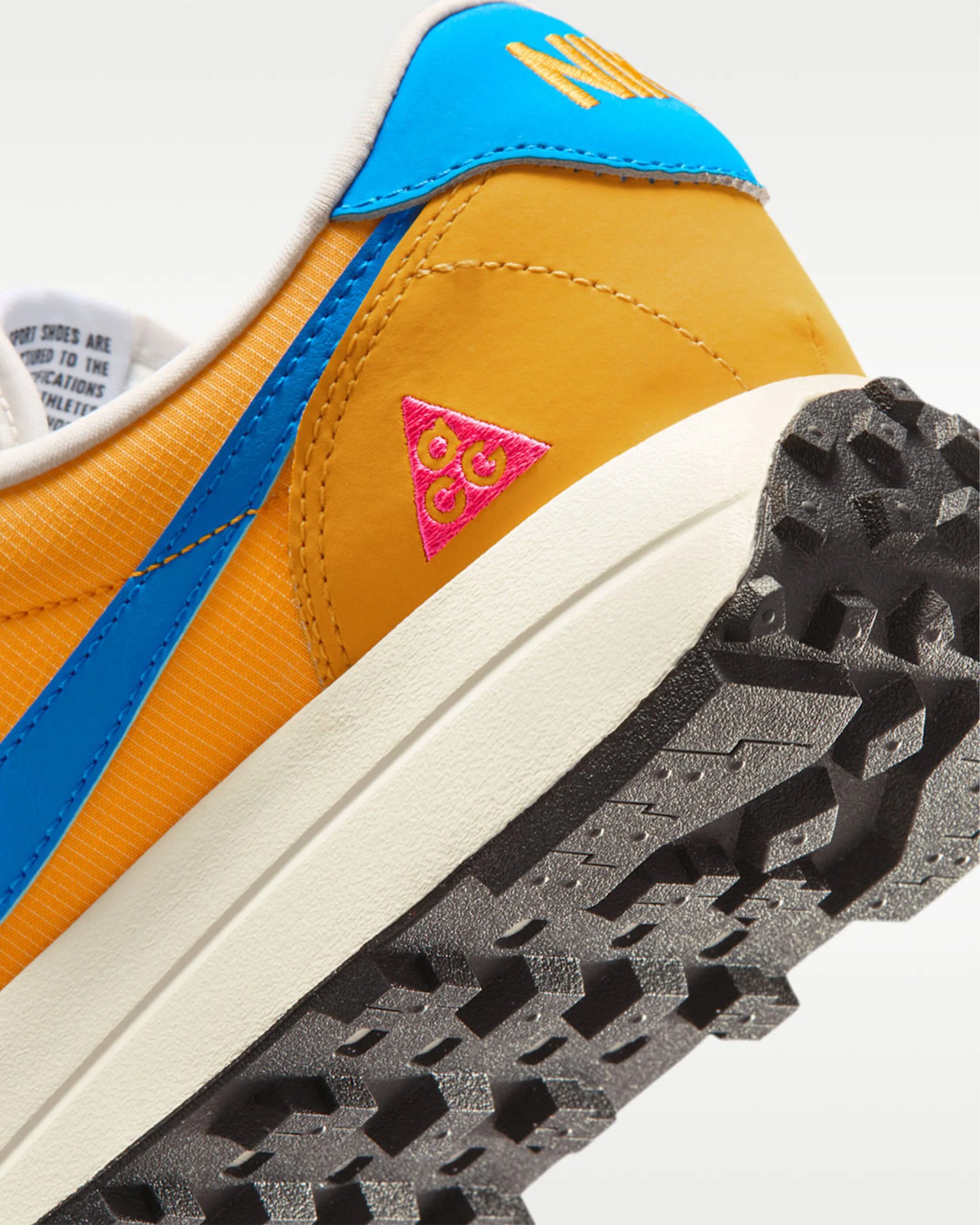 Close-up of a yellow and blue sneaker heel with a pink triangular logo and a textured black sole.