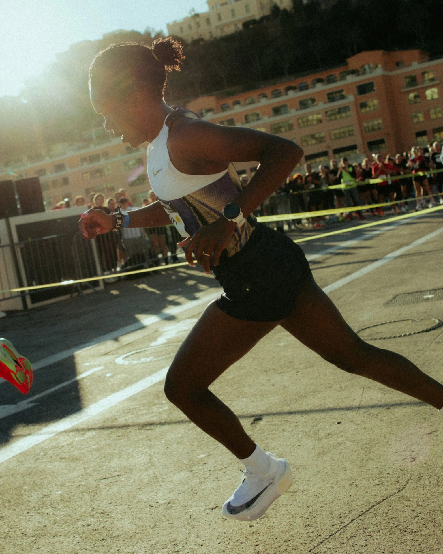 Runner in black shorts and white tank top with a white smartwatch running outdoors on a sunny day.