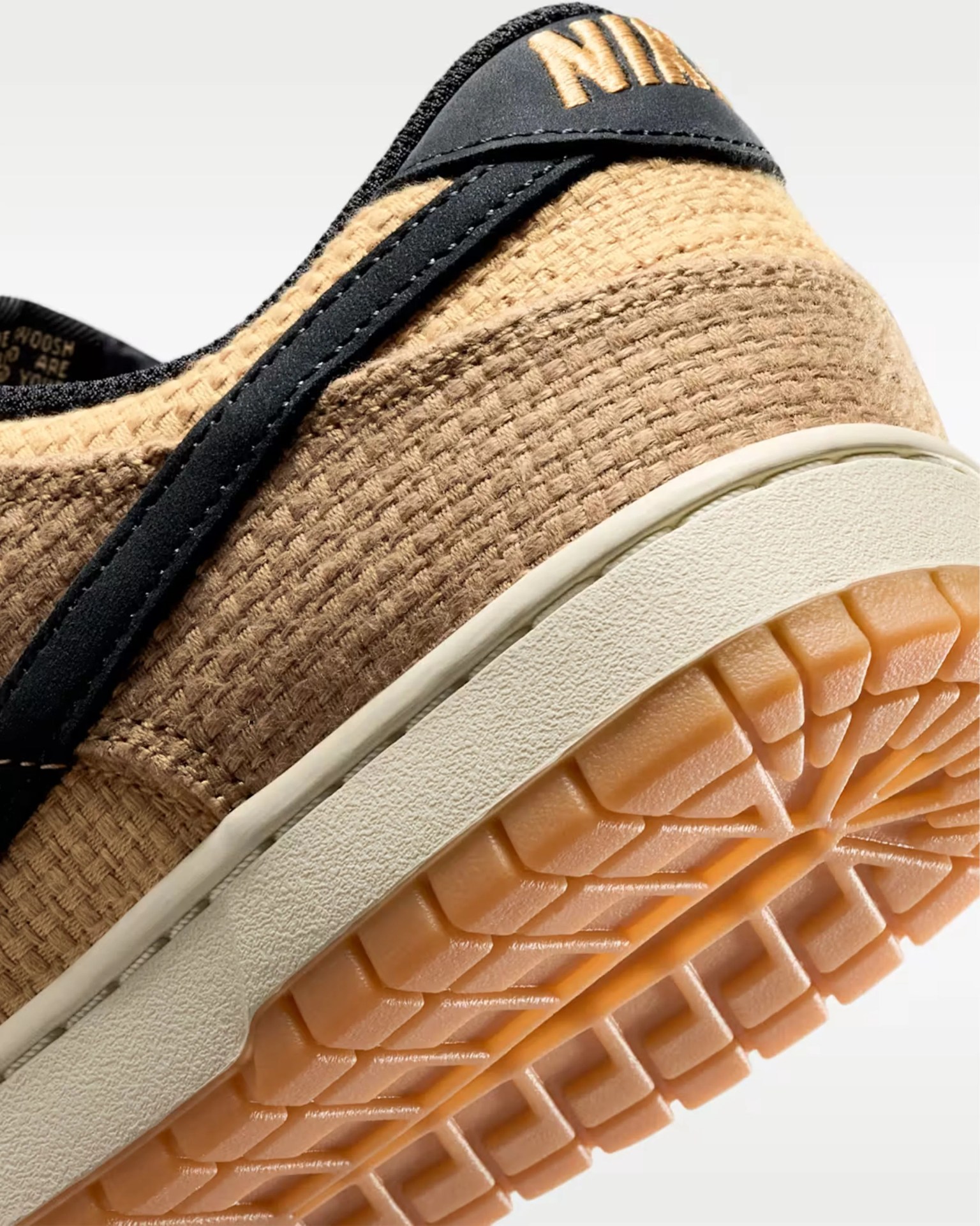 Close-up of the heel and sole of a beige woven Nike sneaker with black accents and a gum rubber outsole.