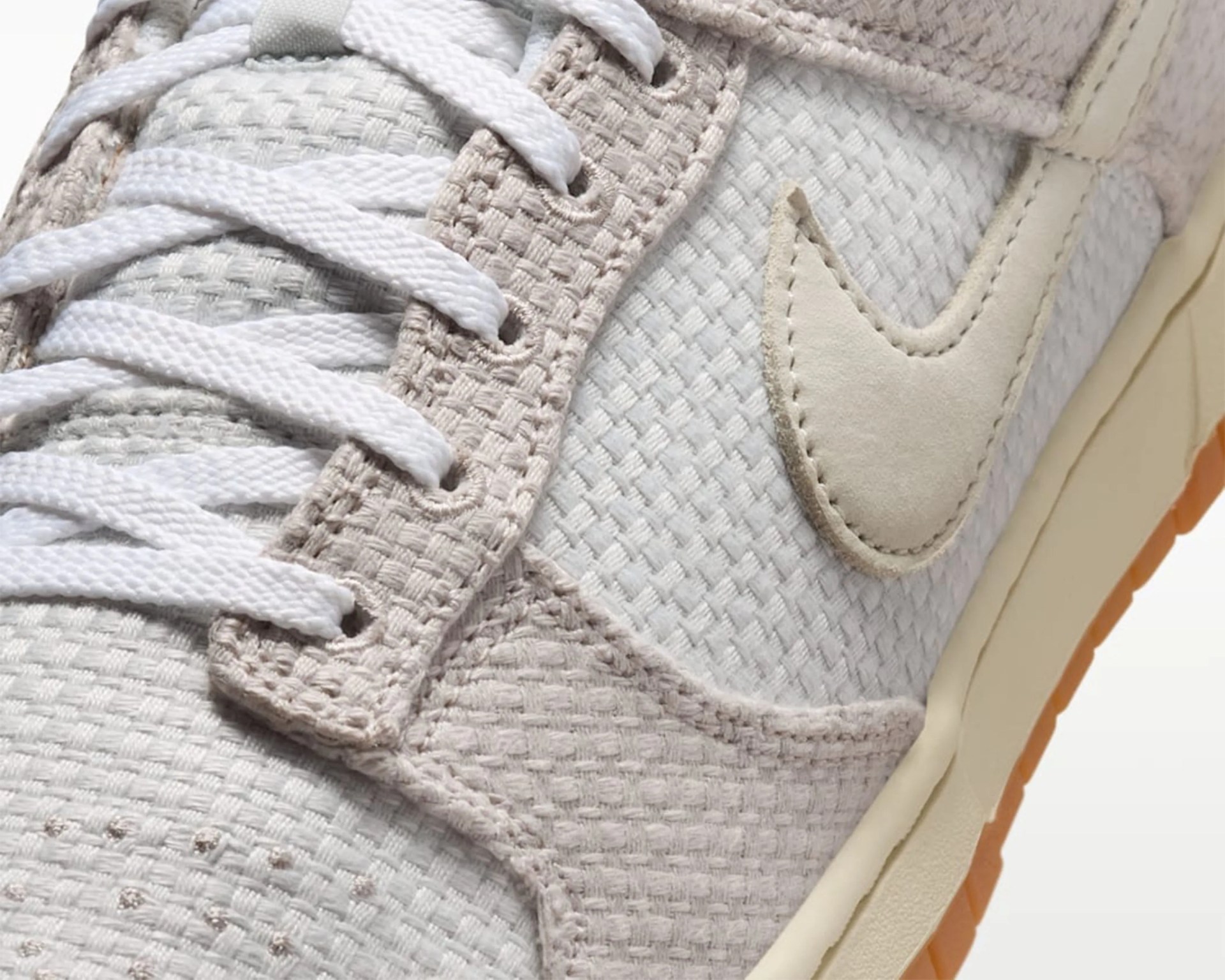 Close-up of a beige and white Nike sneaker with woven fabric, white laces, and a gum sole.