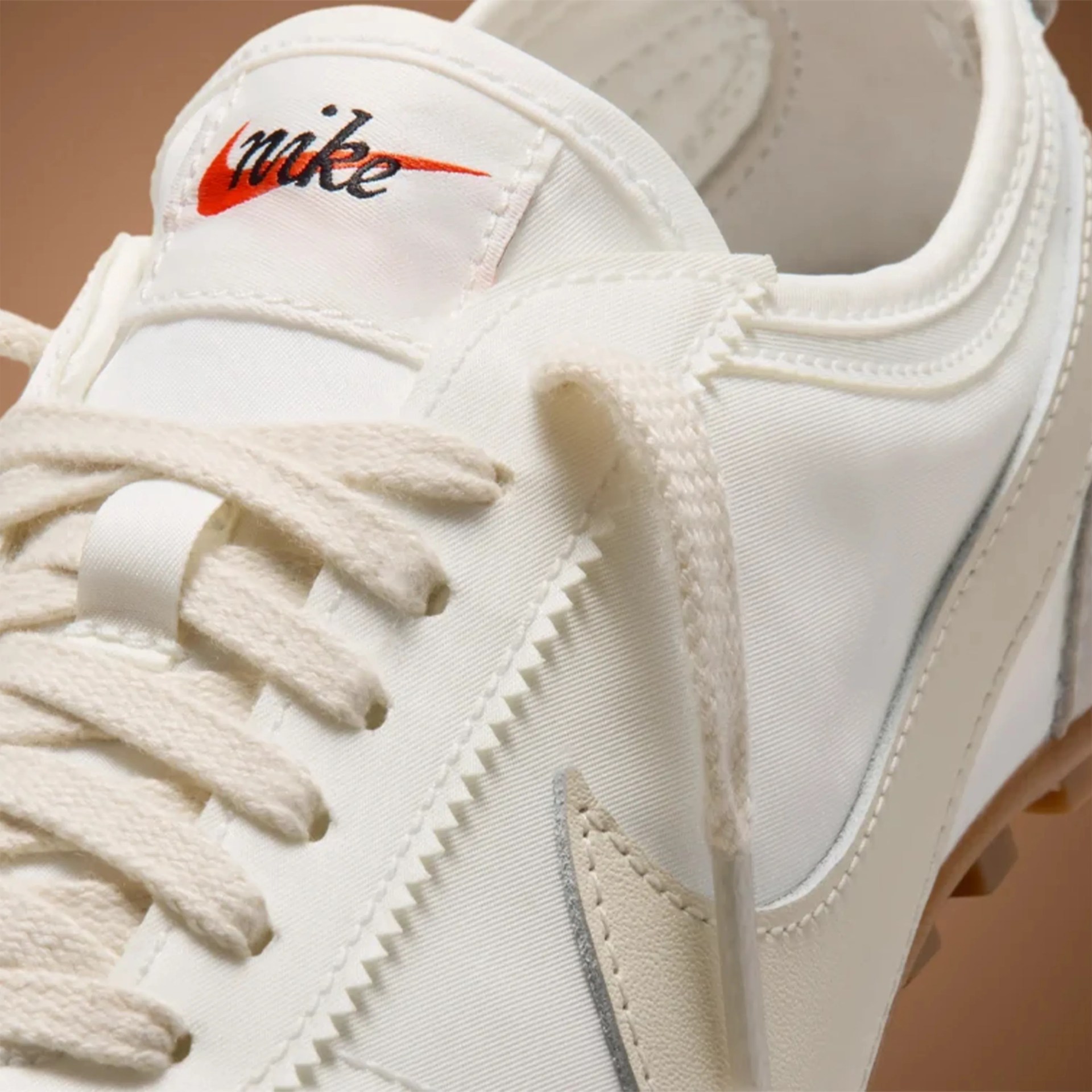 Close-up of a white Nike sneaker with cream laces and an orange Nike logo on the tongue.