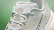 Close-up of a white Nike sneaker with mesh fabric, light beige accents, and white laces against a green background.