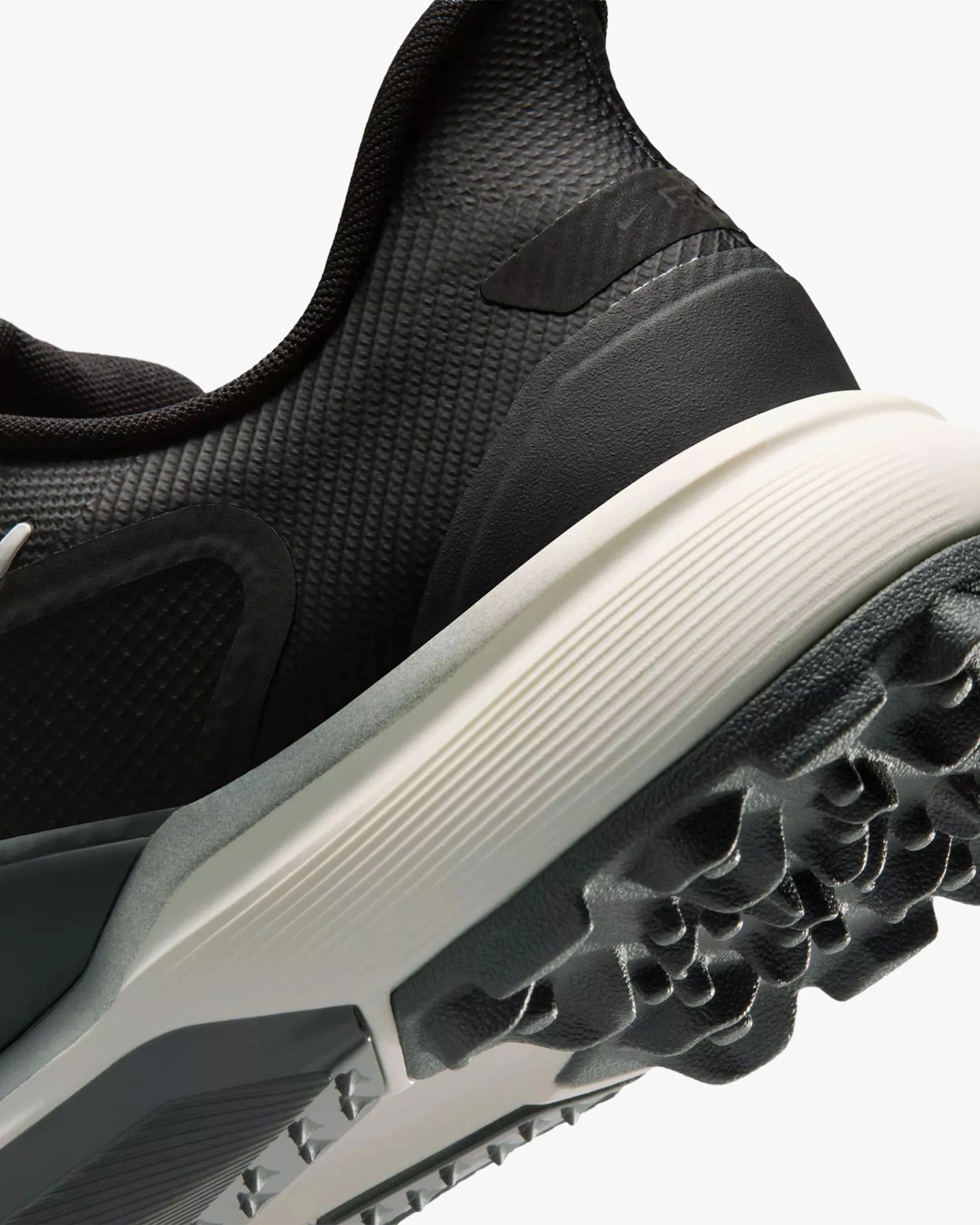 Close-up of a black textured sneaker heel with a white midsole and rugged black outsole.