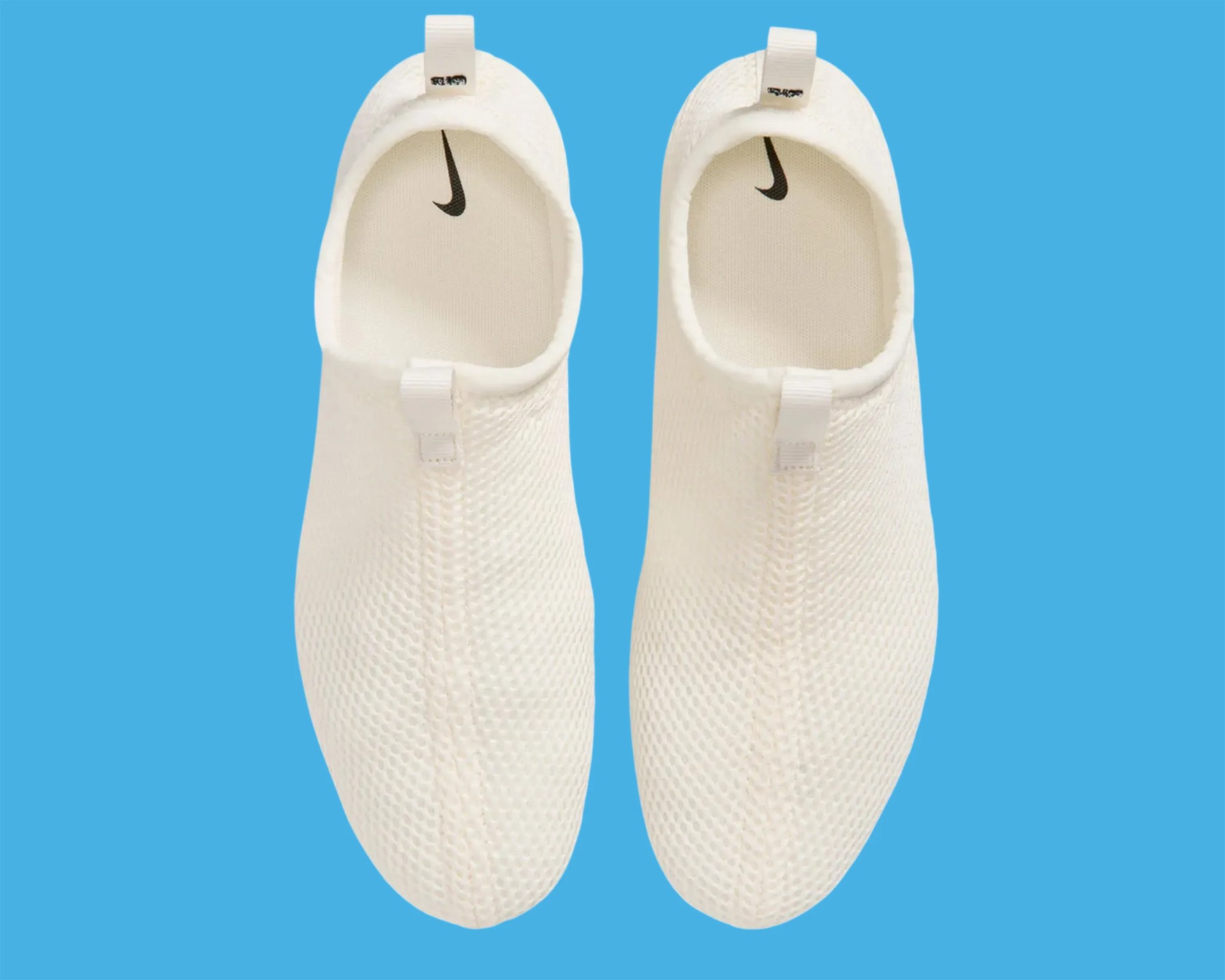Pair of white Nike slip-on shoes with textured mesh upper and black Nike swoosh inside, on blue background.
