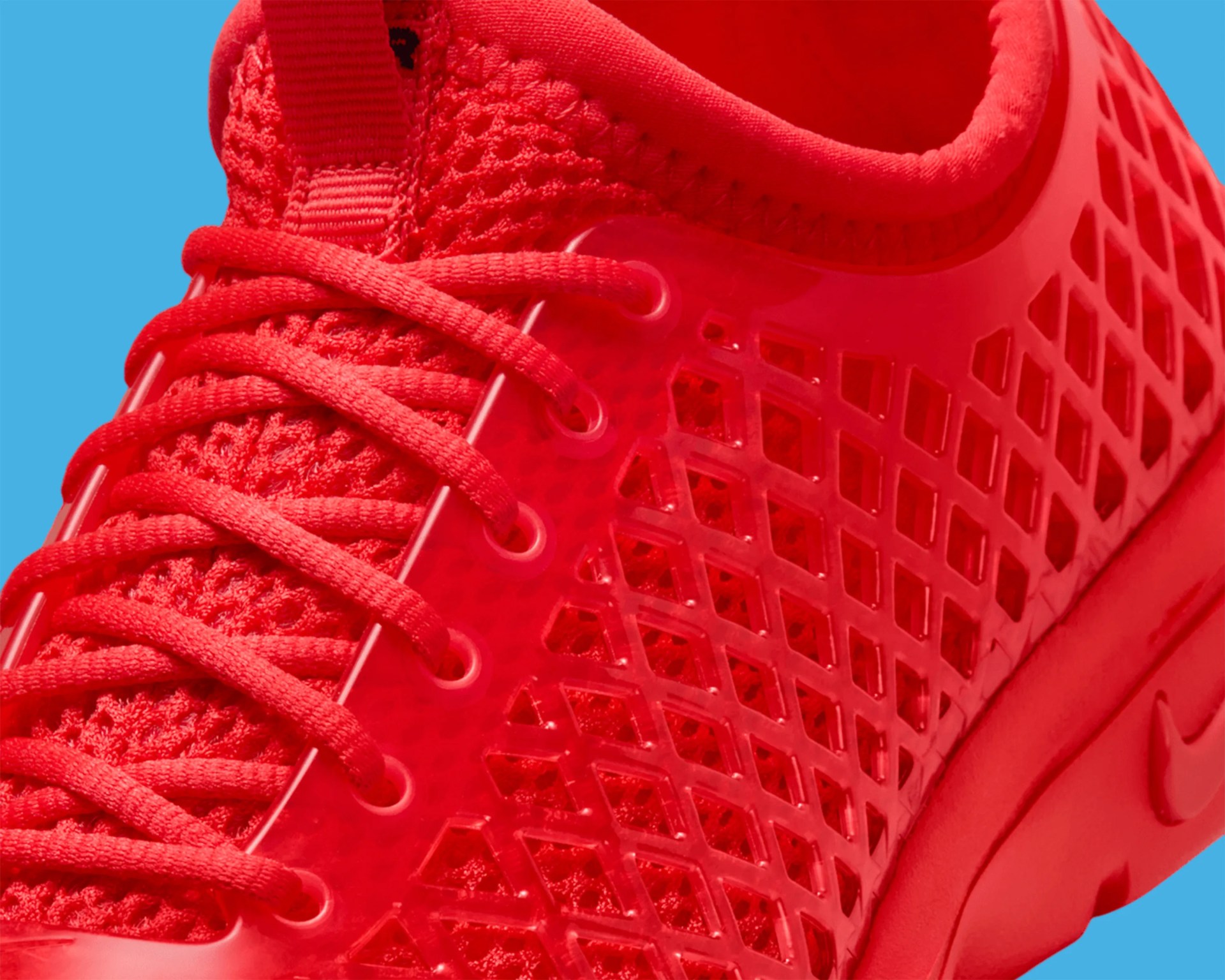 Close-up of a bright red sneaker with mesh fabric and plastic lattice side panel against a blue background.