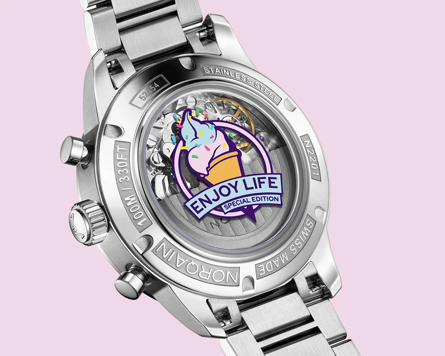 Back of a stainless steel wristwatch with visible mechanical movement and an "Enjoy Life Special Edition" ice cream cone sticker on the glass.