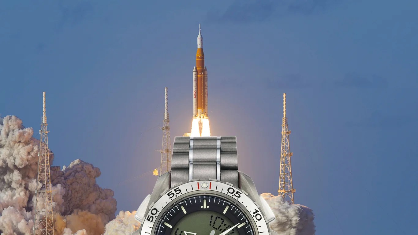 Silver metal digital wristwatch with black face and white bezel in front of a rocket launch.