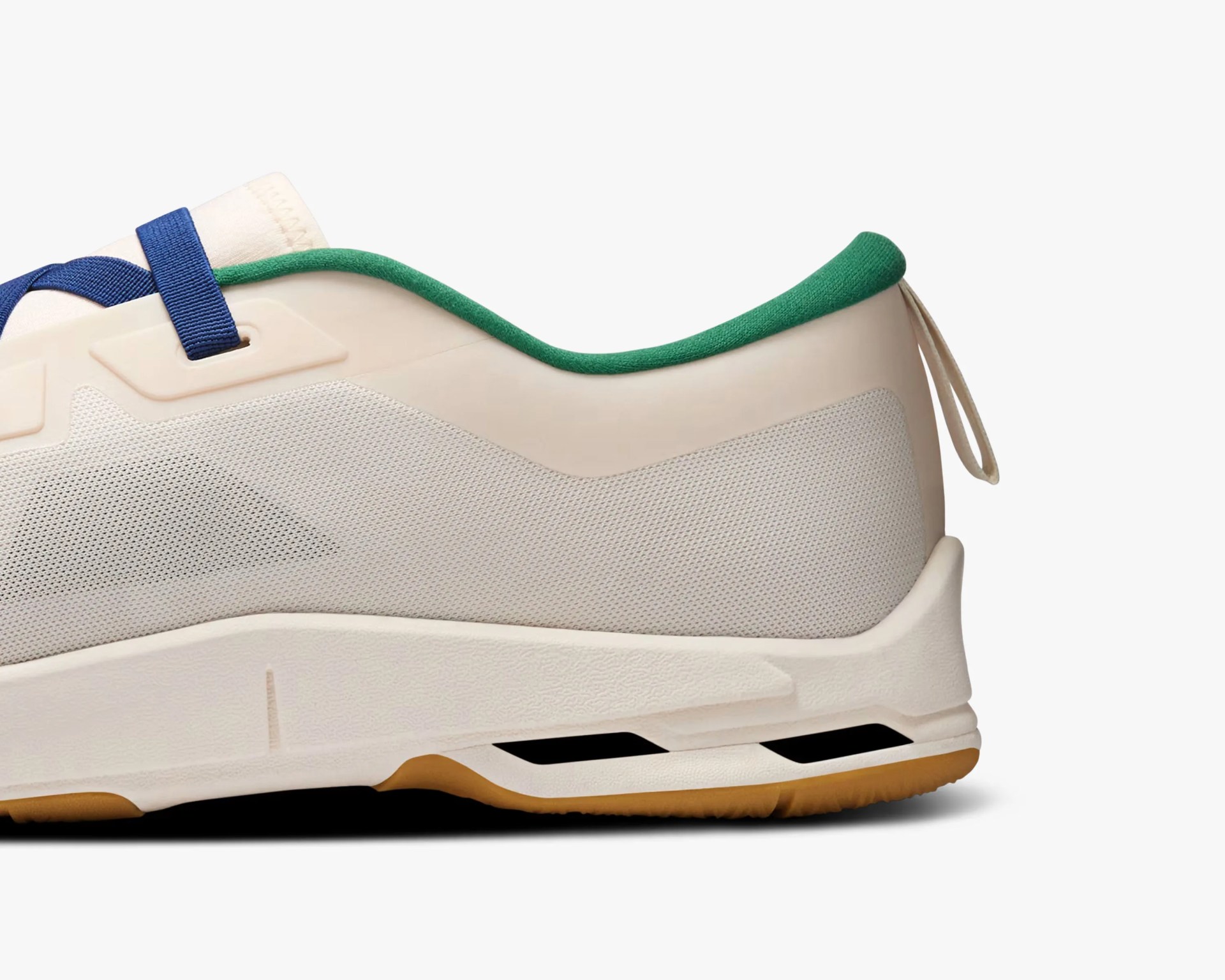 Close-up of the heel and midsole of a beige sneaker with green inner lining, blue laces, and gum sole.