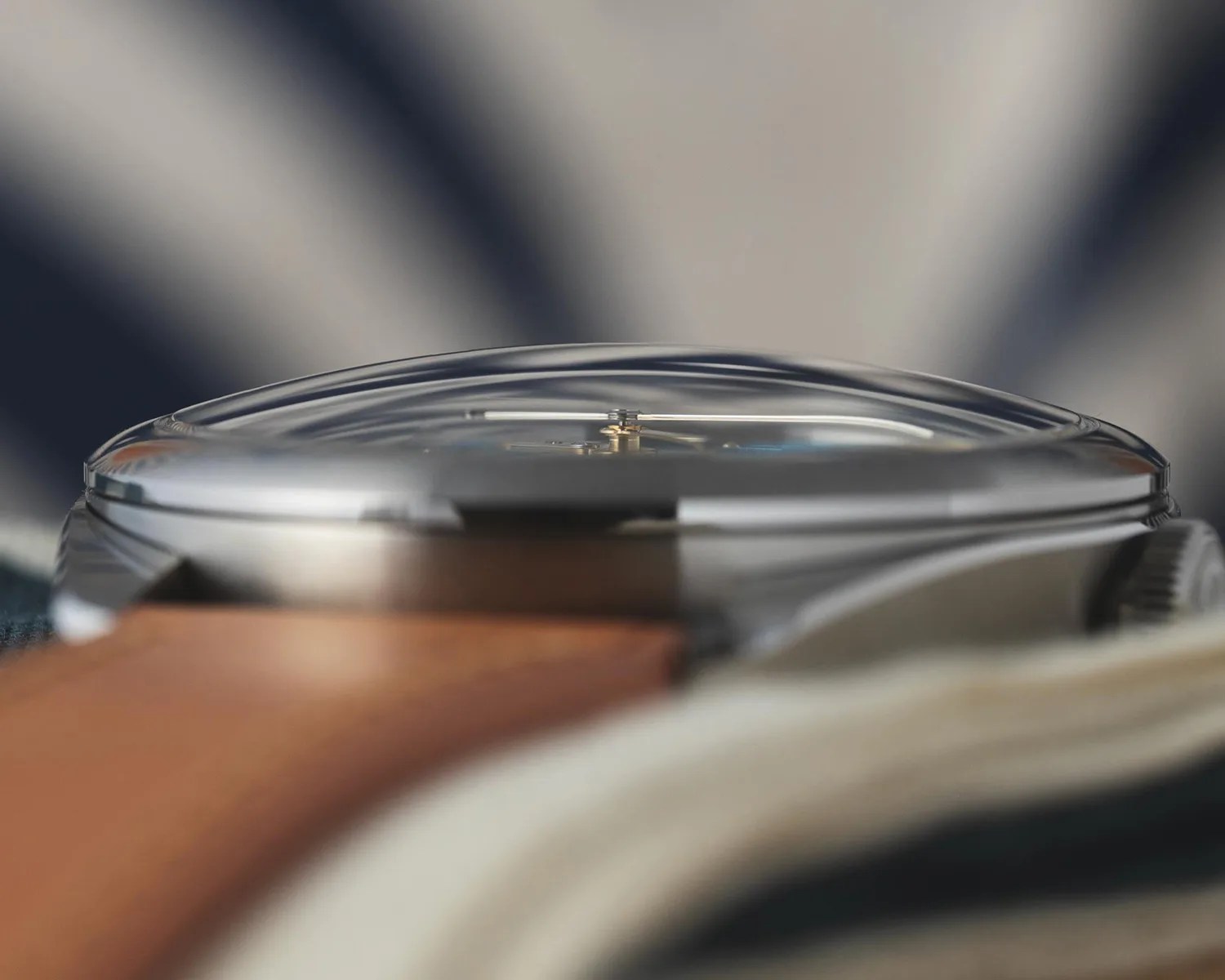Close-up side view of a wristwatch with a domed crystal and a brown leather strap.