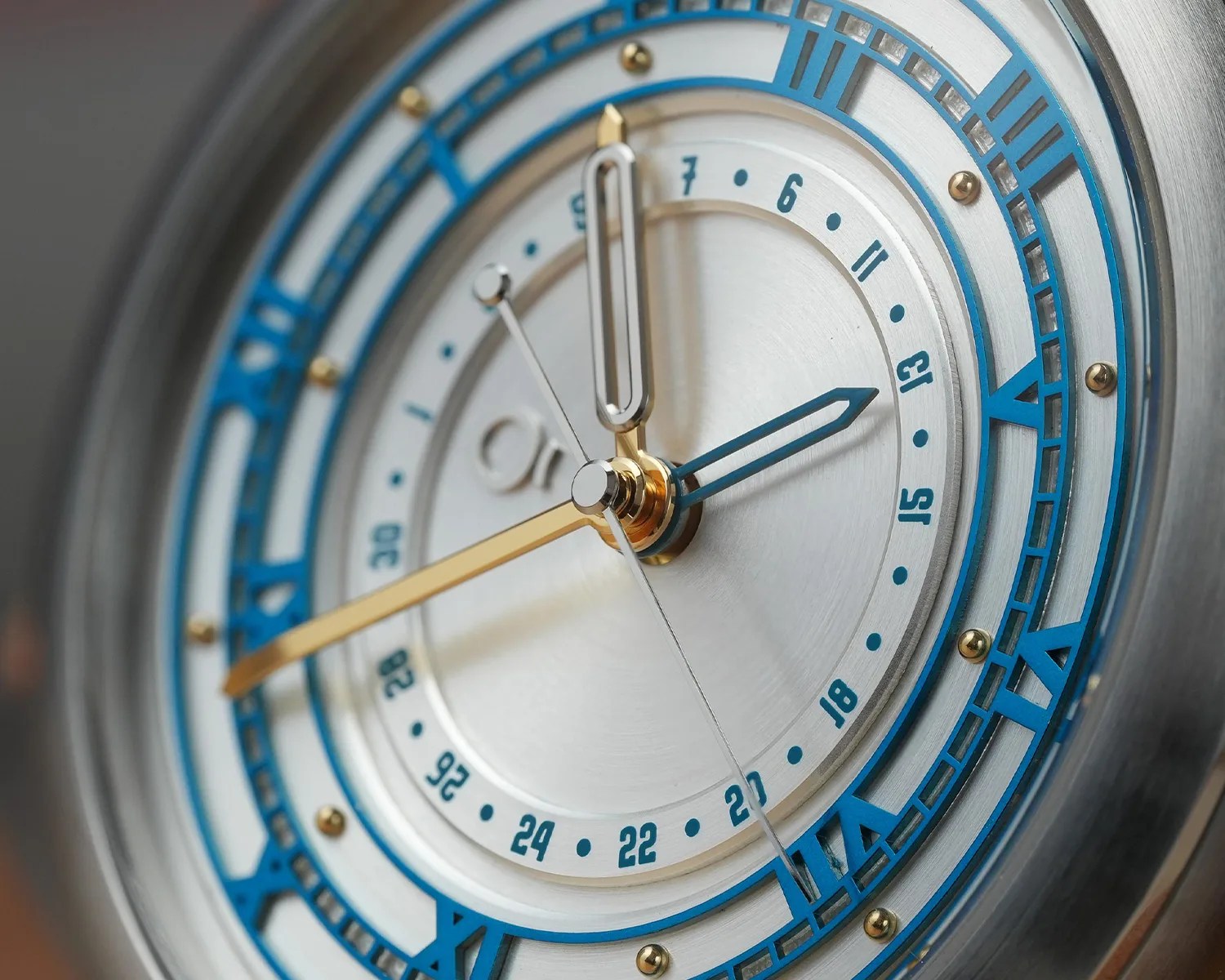 Close-up of a silver watch face with blue Roman numerals, gold accents, and blue and gold hands.