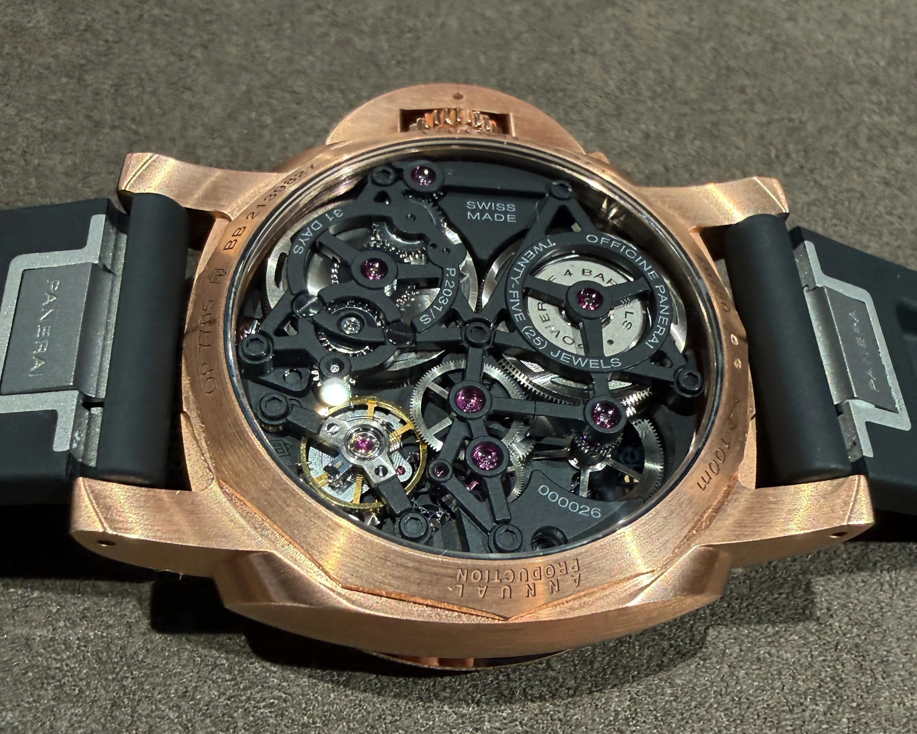 Rose gold watch case back showing intricate black and silver mechanical movement with purple jewels and black rubber strap.