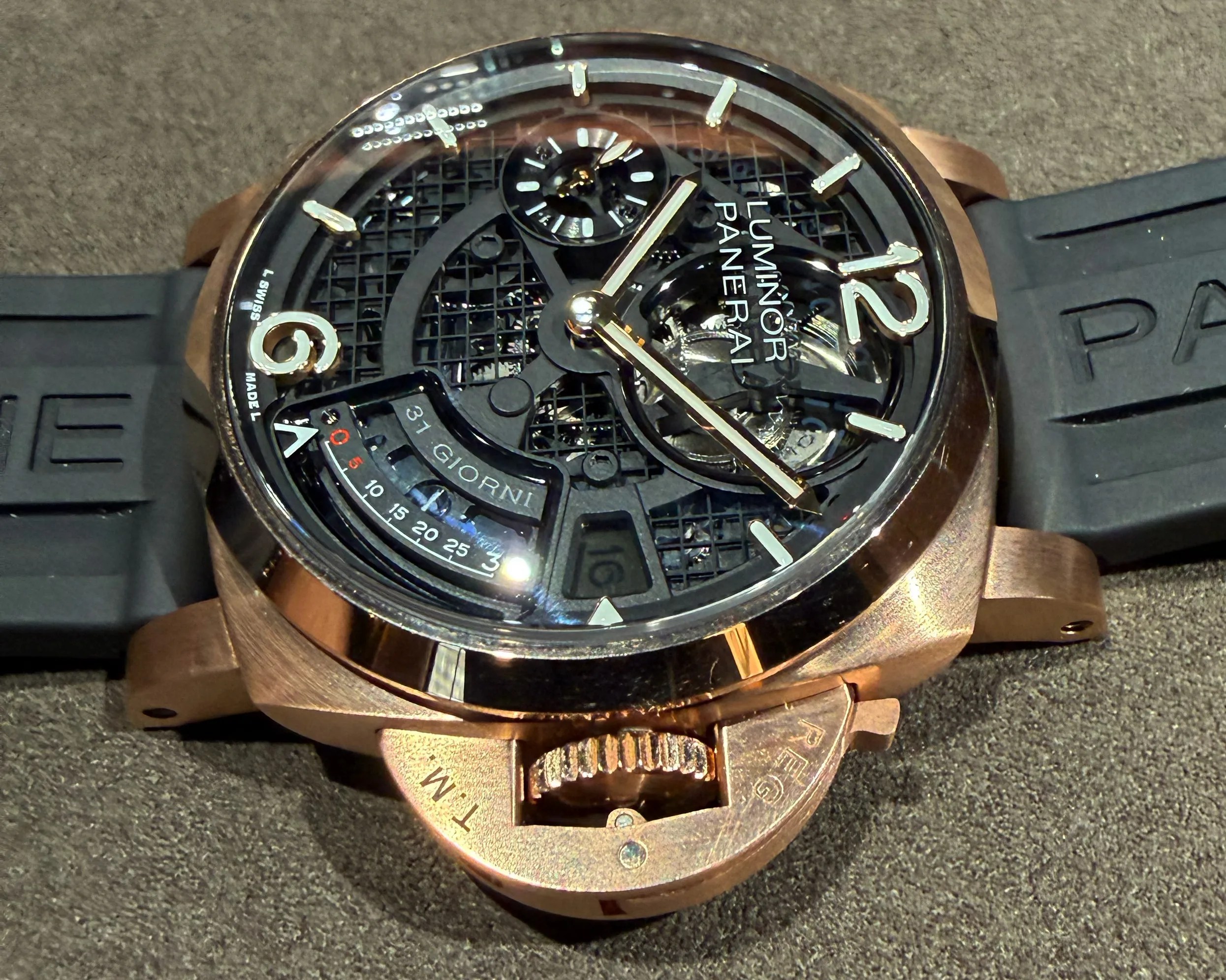 Rose gold Panerai Luminor wristwatch with black skeleton dial and black rubber strap on a textured surface.