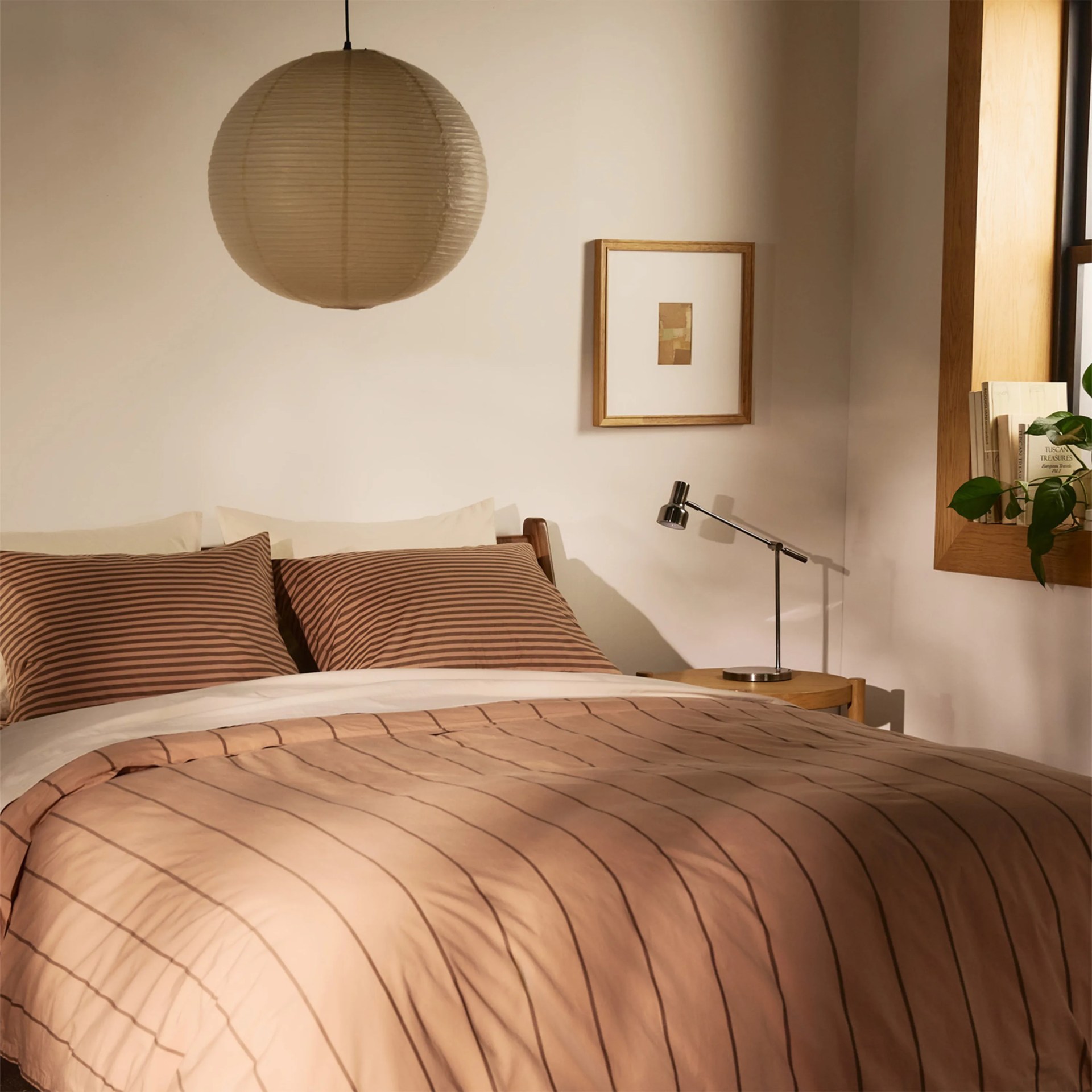 Beige and brown striped bedding on a wooden bed frame with a round paper lantern hanging above.