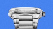 bottom view of a silver stainless steel wristwatch with a ridged bezel and metal link bracelet against a blue background.