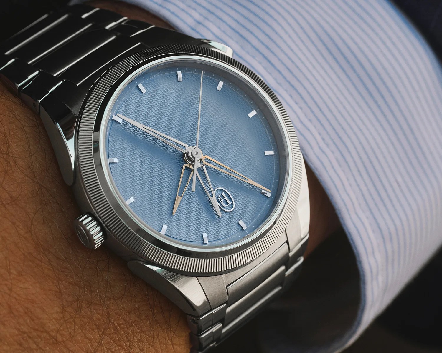 Silver stainless steel wristwatch with a textured light blue dial and silver hour markers worn on a wrist.