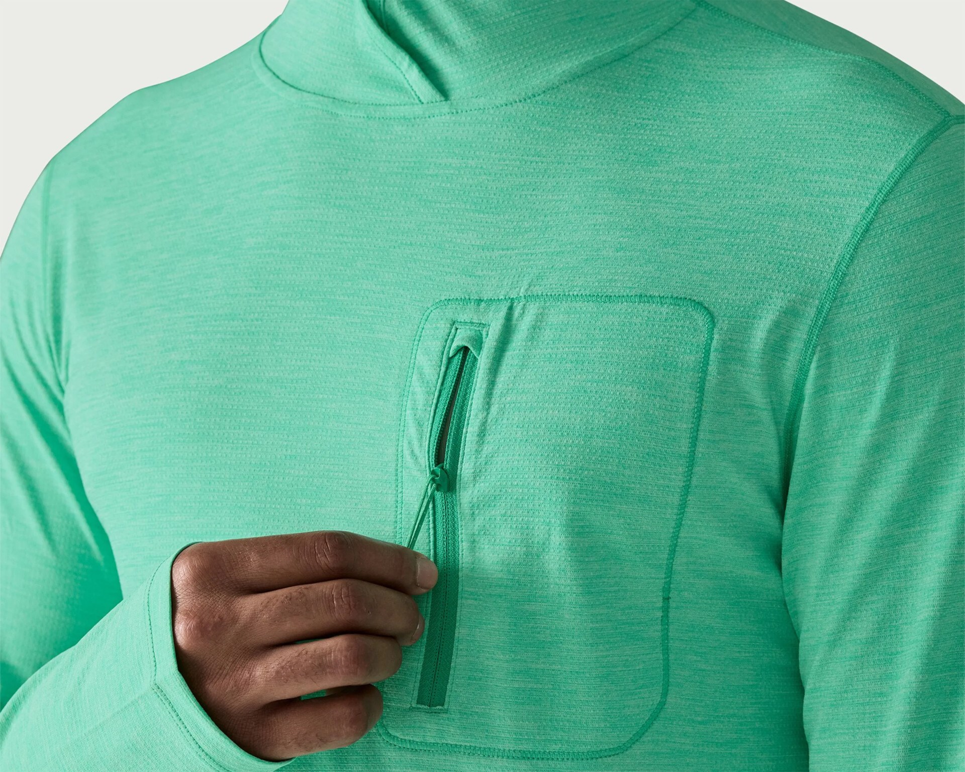 Close-up of a person wearing a mint green hoodie with a zippered chest pocket and thumb hole in the sleeve.