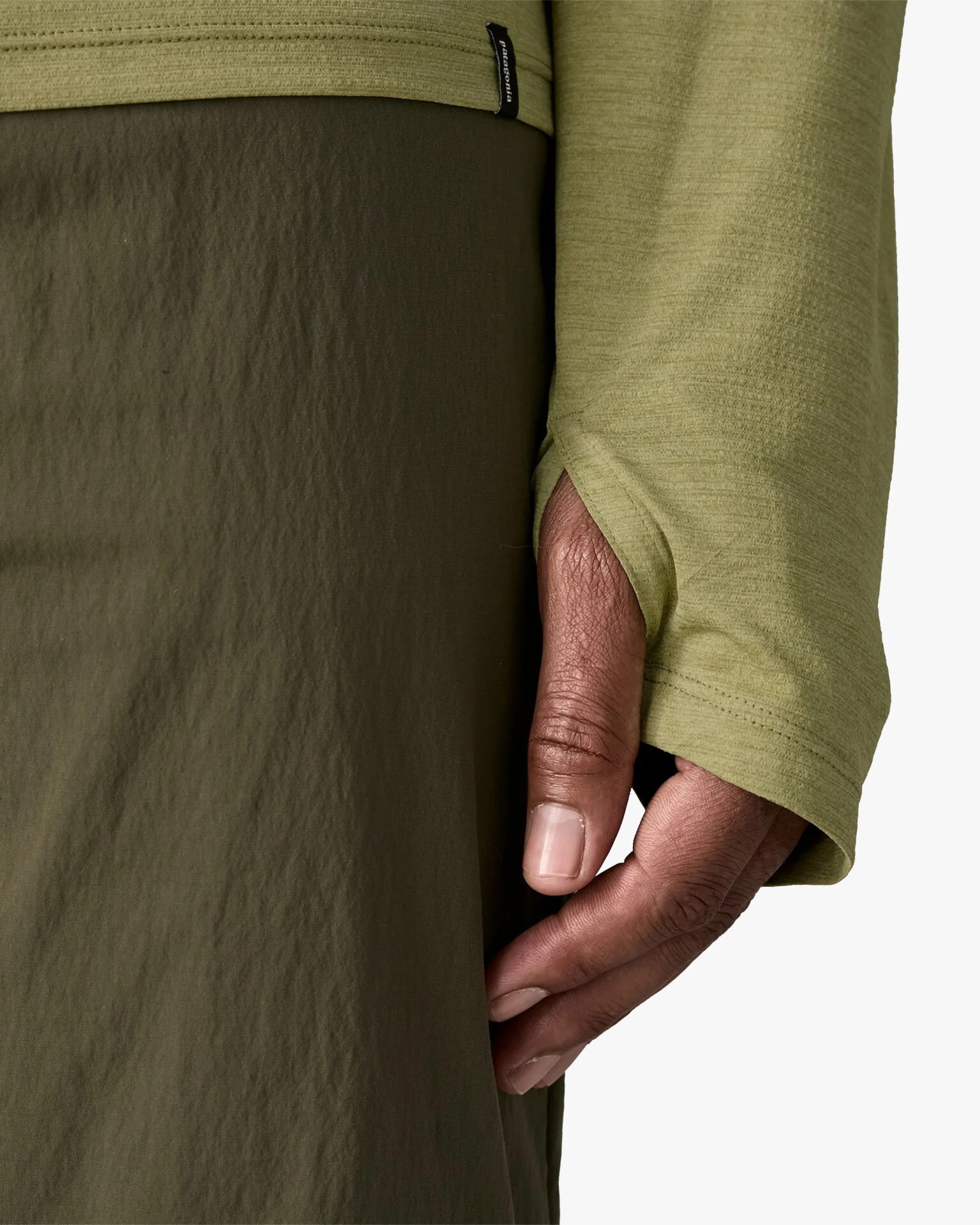 Close-up of a hand partially covered by an olive-green long sleeve with a thumb hole, next to dark olive fabric.