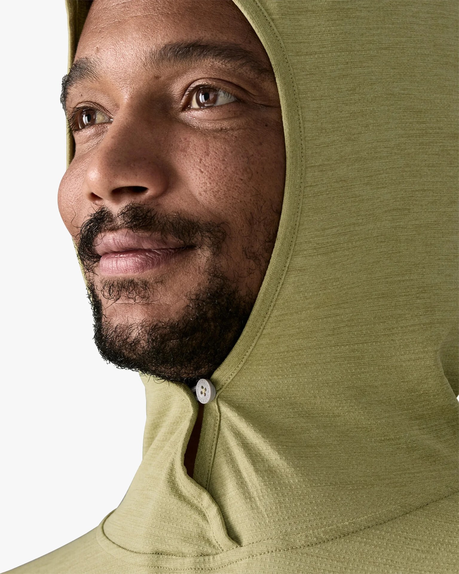 Close-up of a person wearing a light olive green hooded garment with a small white button near the chin.